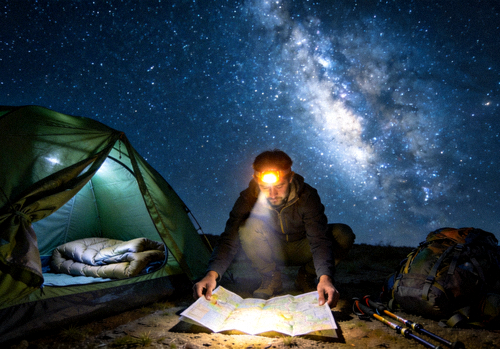 夜晚探险者在星空下的帐篷旁使用头灯查看地图